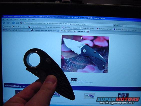 Hand holding a black knife in front of a computer screen showing a Gerber knife