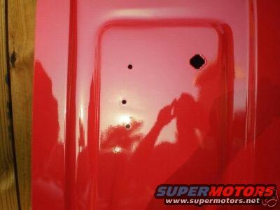 Red tailgate with three holes and a black square hole, reflecting a person holding a camera