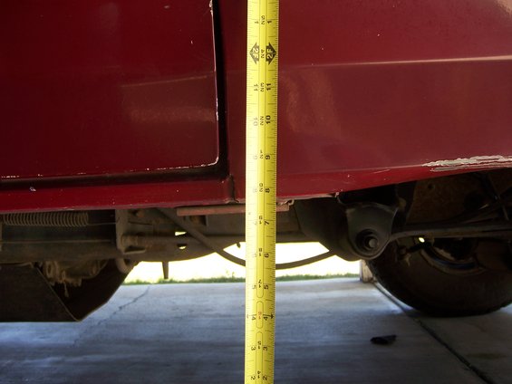 Measuring tape next to the side of a red vehicle, showing suspension components and part of a tire
