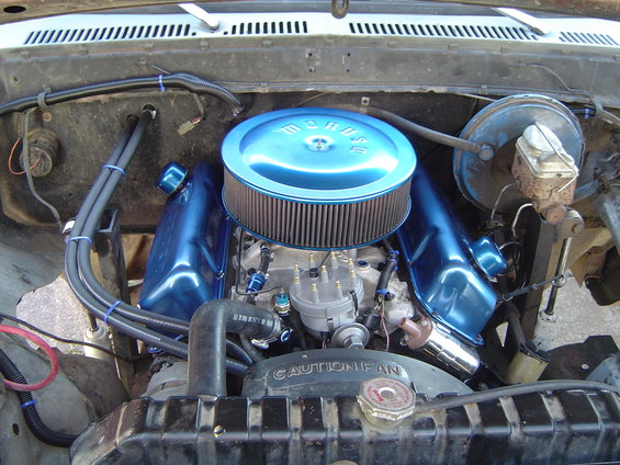 Engine bay with blue valve covers, air cleaner, and radiator. Text on fan shroud reads 'CAUTION FAN'