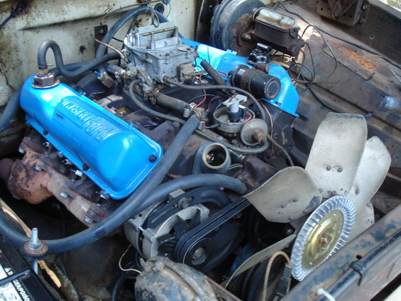 Close-up of a 1967 Ford F-250 engine bay showing blue valve covers, carburetor, and fan