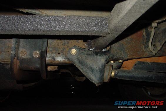 Underside view of vehicle frame with rust and aftermarket sliders attached. Visible bolts and suspension parts
