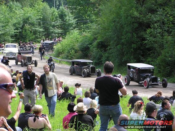 Hot rod cars on a dirt road with spectators watching