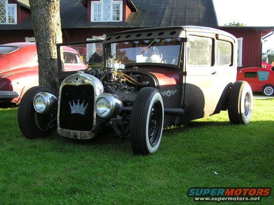 Hot rod with exposed engine, chrome grille with crown emblem, and whitewall tires