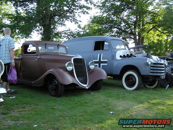 Brown hot rod pickup truck parked next to a grey panel van with a large engine and German cross decal