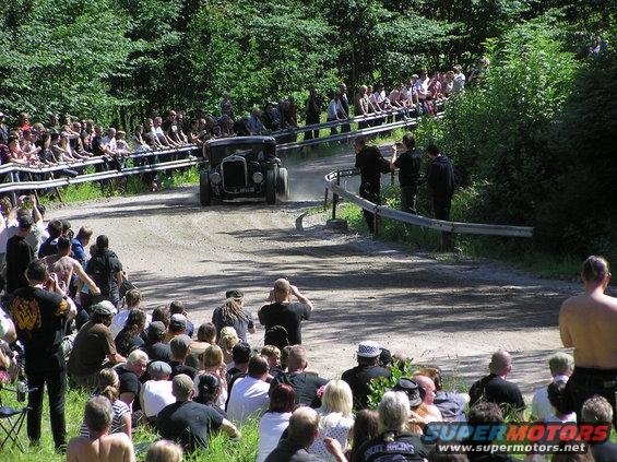 Old car on a dirt track with spectators watching