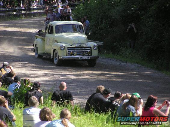 Yellow 1950s GMC pickup truck with a chrome grille and whitewall tires driving on a dirt road