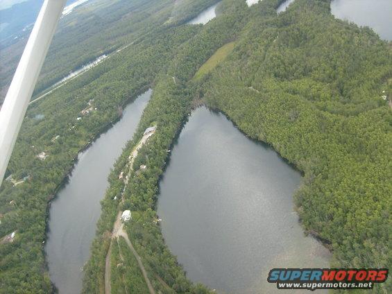 Aerial view of winding lakes and dense green forests, with a few scattered buildings visible along the shorelines
