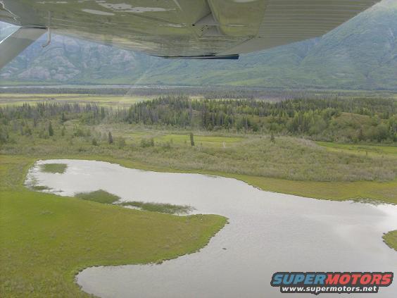 View from an airplane looking out over a lake and wooded hills in Alaska