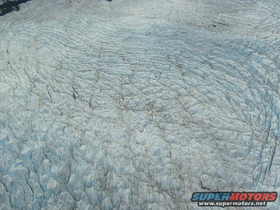 Aerial view of a vast, textured glacier with deep crevasses and ridges