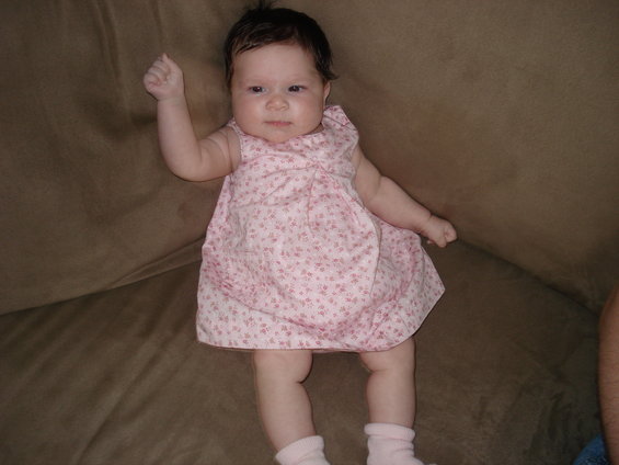 Baby in pink floral dress and pink socks lying on a brown couch