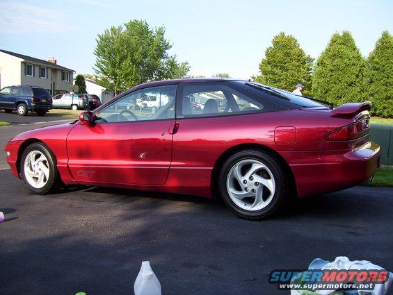 Red coupe parked in a driveway, with a blue SUV and white van in the background