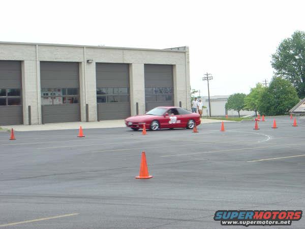 Red 1997 Ford Probe with racing numbers on the door, seen from a 3/4 front angle during a driving event