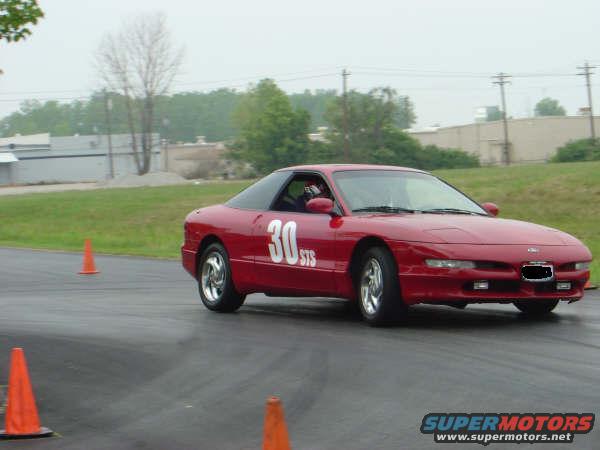 Red sports car with number 30 on the door, driving on a track with orange cones