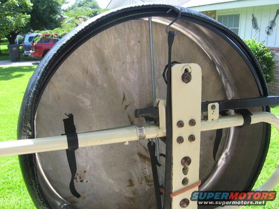 Spare tire carrier mechanism with straps and mounting bracket. Supermotors.net logo visible