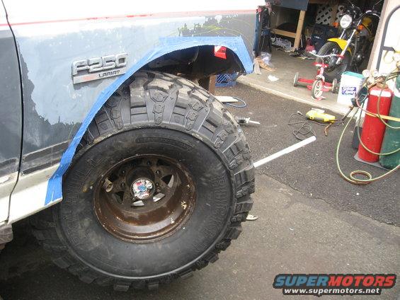 Ford F-250 Lariat fender with blue tape, large off-road tire, and rusty wheel