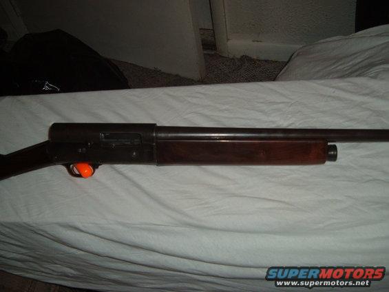 Side view of a shotgun with a wooden stock and an orange trigger guard