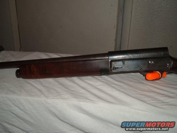 Side view of a shotgun with wooden stock and orange trigger guard