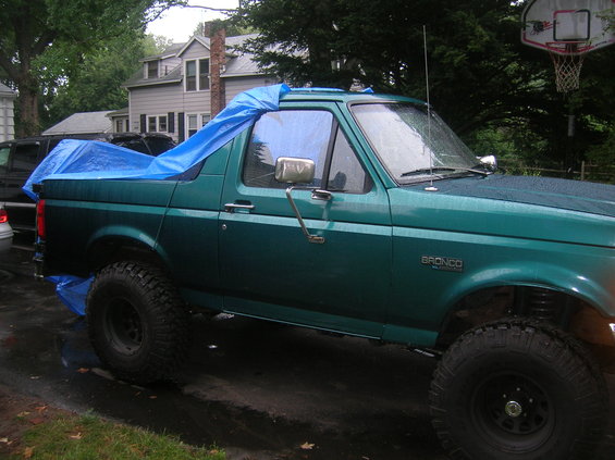 Green Ford Bronco with a blue tarp over the rear, parked outside