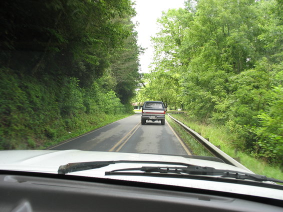 Pickup truck driving on a two-lane road surrounded by trees. View from inside another vehicle