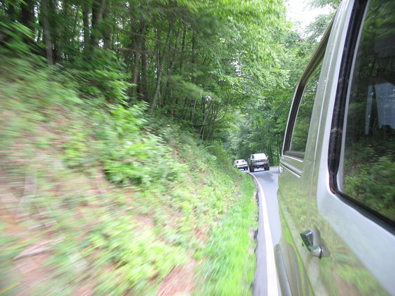 Silver van side view, driving on a tree-lined road with another vehicle ahead