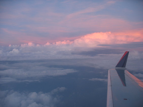 Airplane wing visible against a sky with pink and purple clouds at sunset