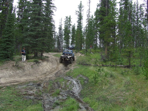 Blue pickup truck driving on a muddy, wooded trail