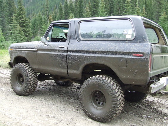 Mud-covered black Ford Bronco with large off-road tires, viewed from the rear three-quarter angle
