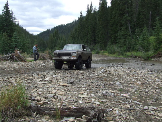 Ford Bronco parked on a rocky stream bed with a person standing nearby