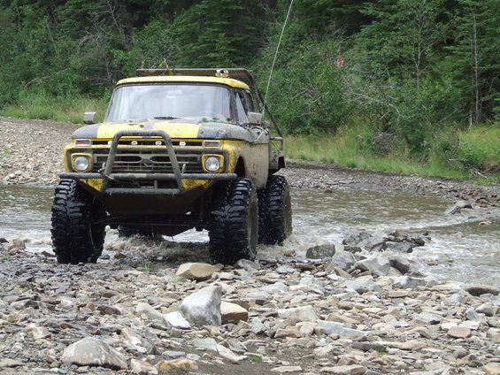 Yellow Ford pickup truck with a brush guard driving through a rocky stream