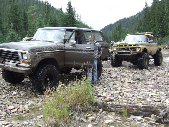 Muddy Ford Bronco parked on rocky terrain with a yellow pickup truck behind it