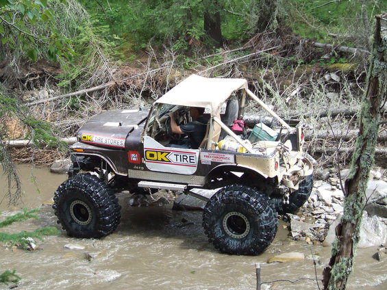 Brown and tan modified Jeep CJ-7 with large tires driving through a stream