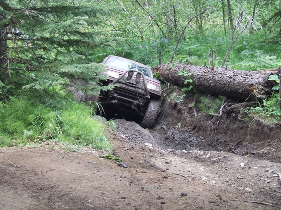 Red off-road vehicle with a brush guard stuck in a muddy ditch, front-left tire off the ground