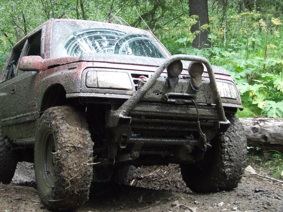 Mud-covered SUV with large tires and a brush guard, parked on a dirt trail