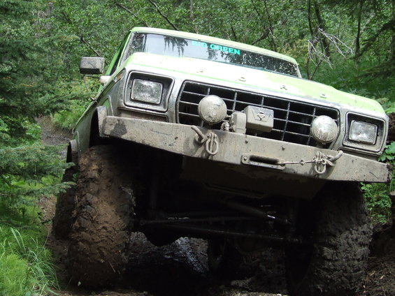Green Ford F-Series truck with large tires on a muddy trail