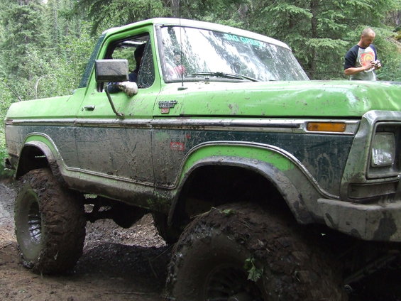 Mud-covered green 1978 Ford Bronco with large off-road tires, seen from a 3/4 front angle