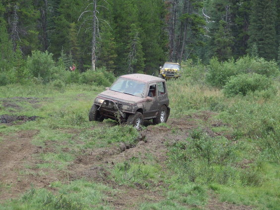 Muddy Suzuki Sidekick navigating a rutted trail with another off-roader behind