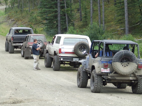 Four-wheel drive vehicles lined up on a dirt road, including a 1990 Ford Bronco