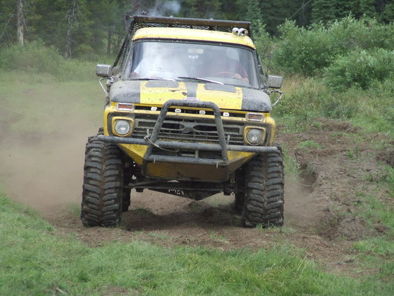 Yellow and black off-road truck with large tires and a bull bar driving on a dirt path