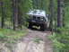 1988 Ford Bronco - Truck navigates a muddy, wooded trail. The grille indicates it is likely a GMC from the 1980s.