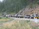 1988 Ford Bronco - A convoy of modified trucks and SUVs travels along a mountain road, with a speed limit sign visible.
