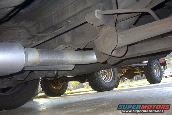 Undercarriage of a vehicle showing a new exhaust pipe and suspension components, with another vehicle visible in the background