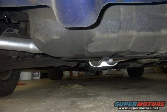 Underside of a car showing the fuel tank and dual exhaust pipes. Tires and part of the blue body are visible