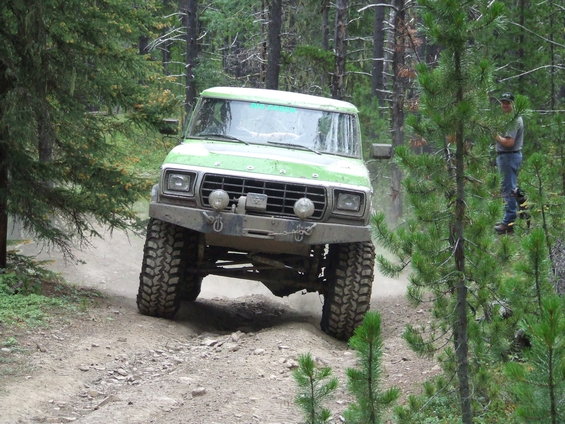 Green off-road truck with large tires driving on a dirt path in a forest