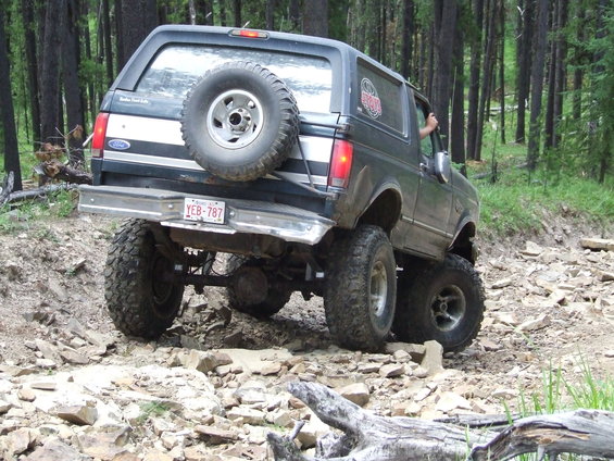 Dark blue Ford Bronco with a spare tire on the back, driving on a rocky trail