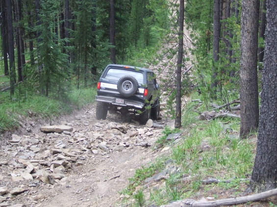 1990 Ford Bronco driving on a rocky, wooded trail