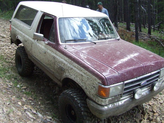 Mud-splattered 1987 Ford Bronco with aftermarket lights on a rocky trail