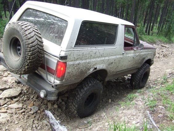Ford Bronco on a dirt road with a spare tire on the back. It's covered in mud