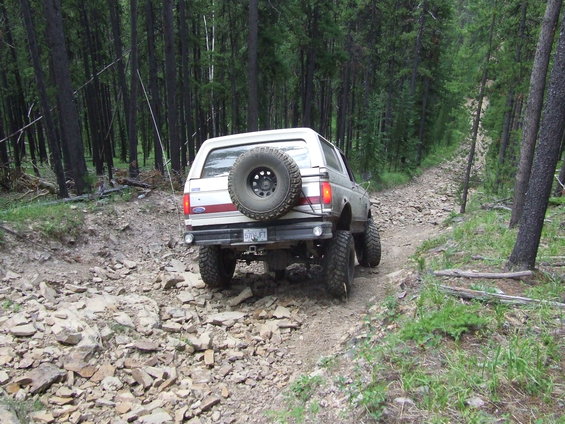 1990 Ford Bronco driving on a rocky, wooded trail