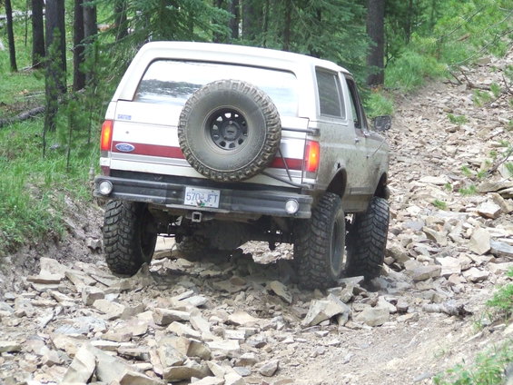 Ford Bronco driving on a rocky trail, spare tire mounted on the back